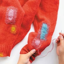 A person repairing torn fabric with a needle and thread.