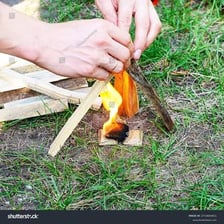 A hand using a flame to light a small fire.