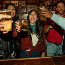 People raising drinks together in a lively bar.