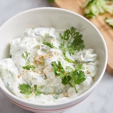 A bowl of creamy raita with cucumber and herbs.