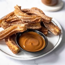 A ridged churro being dipped into dulce de leche.