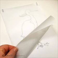 A hand follows the outline of a drawing through a sheet of tracing paper.