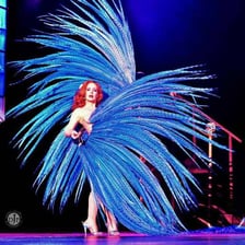 A burlesque performer holding large feather fans.
