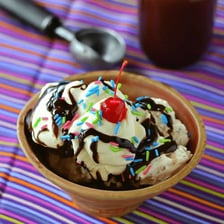 Chocolate fudge sauce is poured over an ice cream sundae.