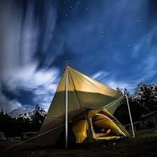 A camping tent standing under a night sky, supported by poles.