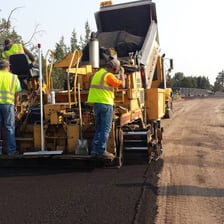A road worker laying pavement across a roadway