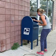 A person putting a letter into a postal mailbox.