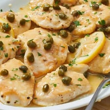 A plate of chicken piccata garnished with lemon