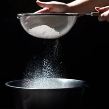 A kitchen sieve being used to sift flour.