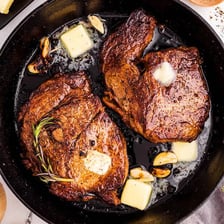 A steak with a browned crust searing in a skillet