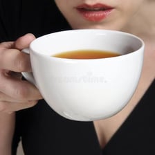A person taking a small, delicate sip from a cup.