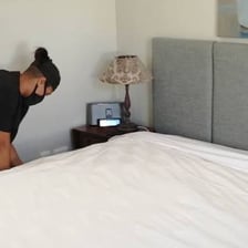 A hotel housekeeper making a bed in a guest room.