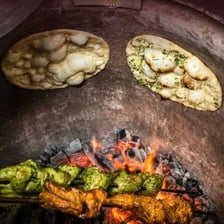 Naan bread being baked in a clay tandoor oven