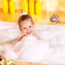 A toddler sitting in a bath surrounded by soap bubbles.