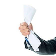 A hand compressing a sheet of paper into a crumpled wad