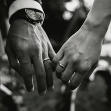 A married couple holding hands with wedding rings visible.