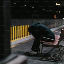 A dejected person sitting alone in a subdued setting.