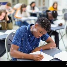 A student working on a written exam at a classroom desk.