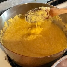 A spoon stirring polenta in a cooking pot