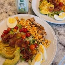 A Cobb salad arranged with lettuce, bacon, chopped egg, chicken, tomato, avocado, and blue cheese.