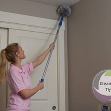 A person using a broom to clear cobwebs from a ceiling.