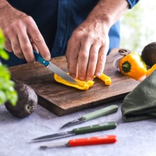 A cook trimming a vegetable with a kitchen knife.