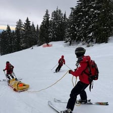 Ski patrollers skiing down a marked trail on a mountain.