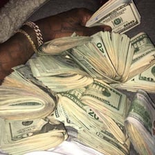 A hand holding several thick wads of dollar bills.
