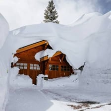 A house is surrounded and partly covered by deep snow.