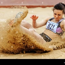 A long jumper landing in the sand pit at the end of a runway.