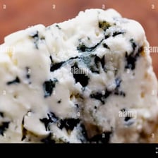 A cut piece of blue cheese shows blue-green mold veins running through it.
