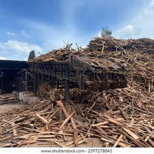 A sawmill with piles of bark and waste bins nearby.