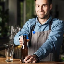 A bartender removing a bottle cap with an opener