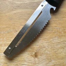 A close-up of a knife blade with repeated sawlike teeth.
