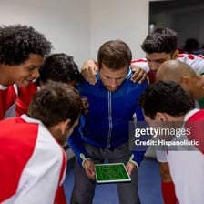A coach discusses strategy with players in a locker room.