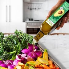 Avocado oil in a bottle beside a bowl of avocados.