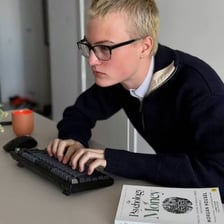 A person with glasses working beside books and a computer.