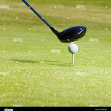 A golf ball perched on a tee beside a driver club.