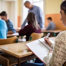 A student writing an essay at a classroom desk.