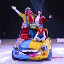 A small circus car with several clowns emerging from it