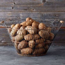 A basket filled with whole potatoes.