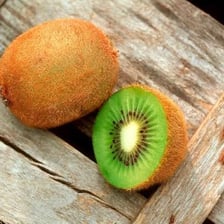 A whole fuzzy brown kiwi beside a sliced kiwi showing its green flesh.