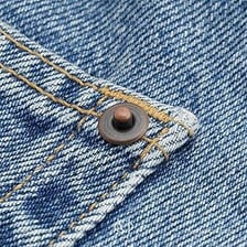 A close-up of a metal rivet on aircraft skin and denim fabric