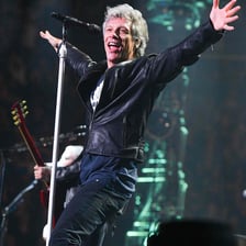 Jon Bon Jovi performing with a microphone at a rock concert.