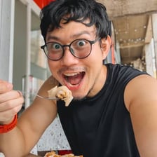 A person smiling while enjoying a bite of food.