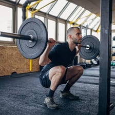 A person performing a barbell squat in a gym.