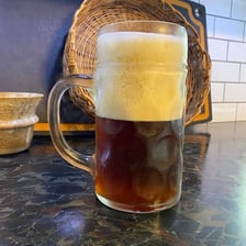 A glass of beer with a thick foamy head beneath a tap