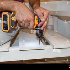 A carpenter using a cordless drill to make a hole in a wooden board