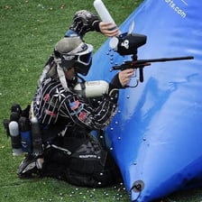 A paintball player reacting dramatically after being struck.