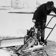 A long-handled saw cutting through ice on a frozen lake